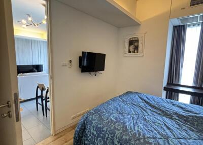 Bedroom with blue bedding, wall-mounted TV, view into adjoining room