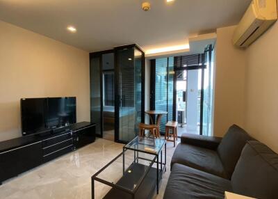 Modern living room with a glass partition, TV unit, black sofa, and small dining area.