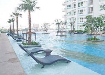 Modern high-rise apartment building with outdoor swimming pool featuring sun loungers and palm trees.