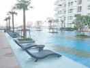 Modern high-rise apartment building with outdoor swimming pool featuring sun loungers and palm trees.