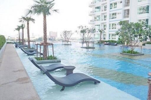 Modern high-rise apartment building with outdoor swimming pool featuring sun loungers and palm trees.