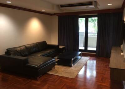 Modern living room with black leather sectional sofa, coffee table, and large window with balcony view