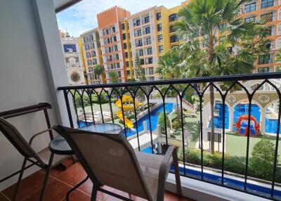 A balcony overlooking an outdoor space with a colorful building and a playground featuring a slide and a pool