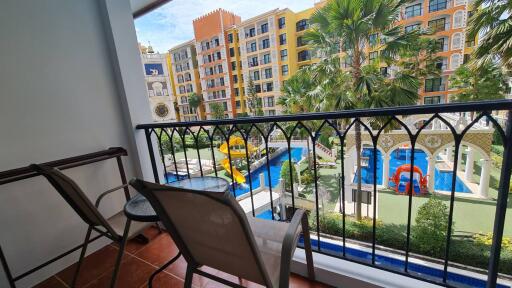 A balcony overlooking an outdoor space with a colorful building and a playground featuring a slide and a pool