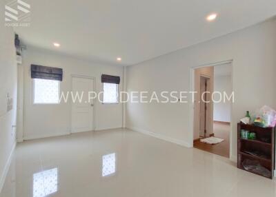 Spacious white-walled living room with small shelving unit and doorway to another room