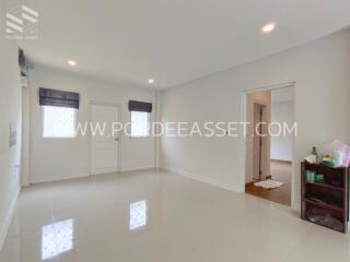 Spacious white-walled living room with small shelving unit and doorway to another room