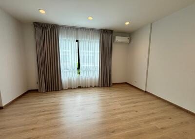 Spacious empty bedroom with large window, curtains, and wooden floor