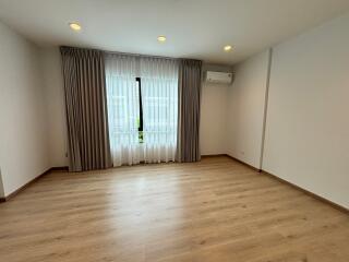 Spacious empty bedroom with large window, curtains, and wooden floor