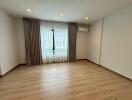 Spacious empty bedroom with large window, curtains, and wooden floor