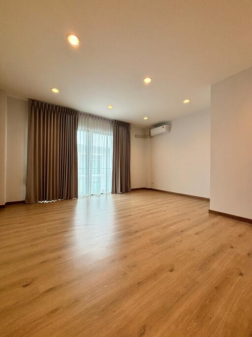 Spacious living room with wooden flooring, large window, and ceiling lights