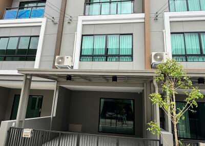 Exterior view of a modern townhouse building with balconies and a gated entrance.