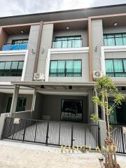 Exterior view of a modern townhouse building with balconies and a gated entrance.