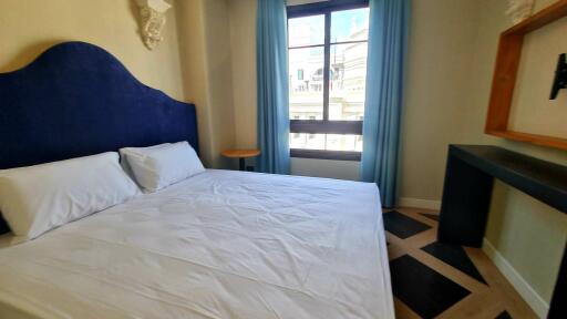 Well-lit bedroom with a large bed, window, and a desk