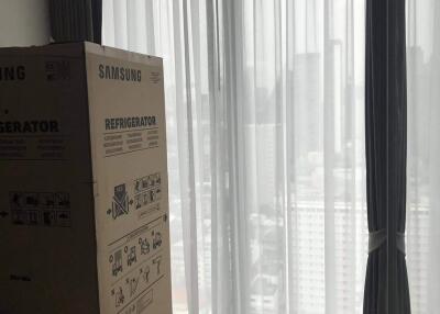 Bedroom with a large window, curtains, and a boxed refrigerator