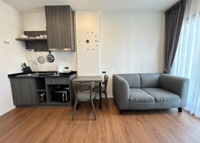 Modern living room and kitchen area with wooden floors, gray furniture, dining table, and large window