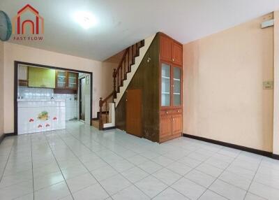 Living room with tiled floor, adjacent kitchen, built-in wooden stair storage, and ample lighting.