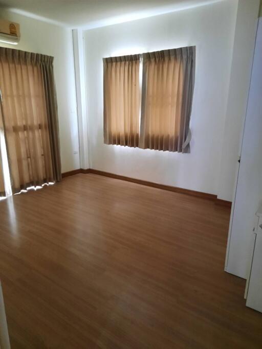 Bright bedroom with wooden flooring and curtains on the windows