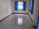 Spacious bedroom with tiled flooring and blue curtains