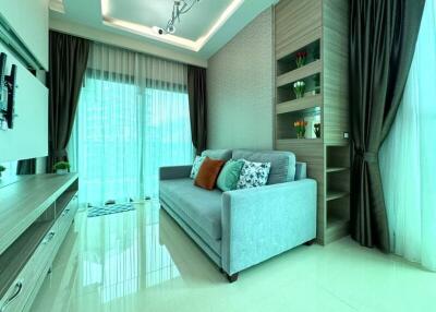 Modern living room with a comfortable sofa, large windows with sheer curtains, and decorative shelves