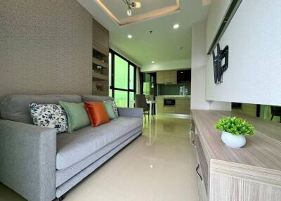 Modern living room with sofa, wall-mounted TV, and open kitchen in the background