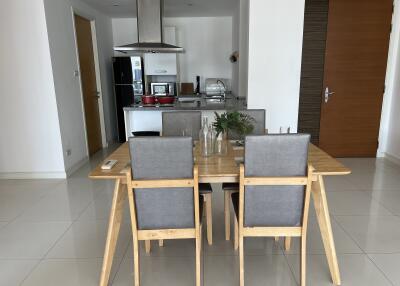 Modern dining area with wooden table and grey chairs adjacent to a kitchen