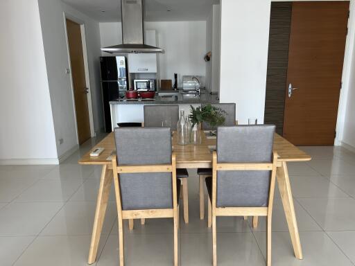 Modern dining area with wooden table and grey chairs adjacent to a kitchen