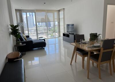 Modern living room with a dining area, black sofa, and large windows providing a city view