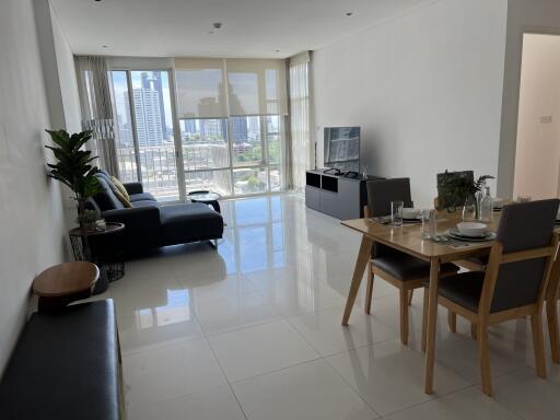 Modern living room with a dining area, black sofa, and large windows providing a city view