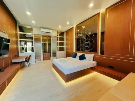 A modern, spacious bedroom with a large bed, built-in furniture, and warm lighting