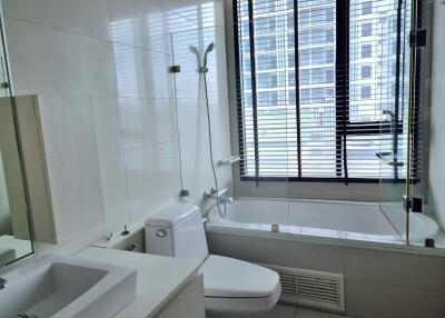 Modern bathroom with a bathtub, shower, toilet, and large window with blinds