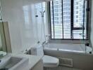 Modern bathroom with a bathtub, shower, toilet, and large window with blinds