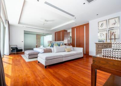 Spacious and modern bedroom with wooden floor, large windows, a bed, and a seating area.