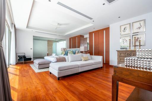 Spacious and modern bedroom with wooden floor, large windows, a bed, and a seating area.