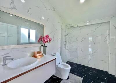 Modern bathroom with marble walls and black floor, featuring a walk-in shower and sink with mirror