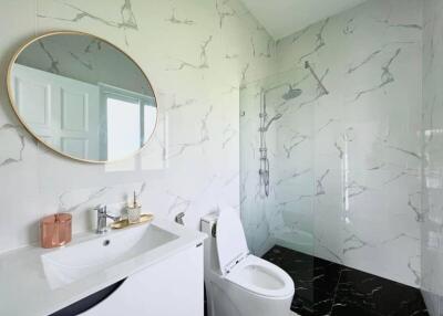 Modern bathroom with marble walls, round mirror, glass shower, and white fixtures