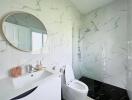 Modern bathroom with marble walls, round mirror, glass shower, and white fixtures