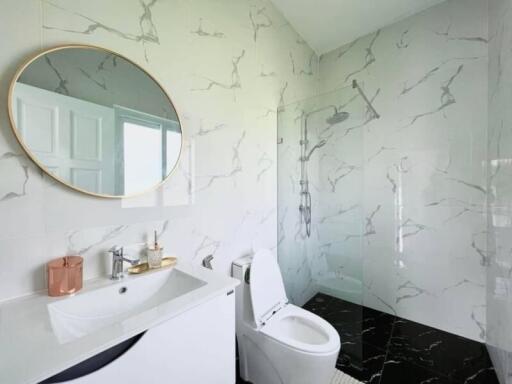 Modern bathroom with marble walls, round mirror, glass shower, and white fixtures