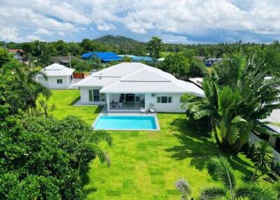 Aerial view of a white house with a pool and a green lawn