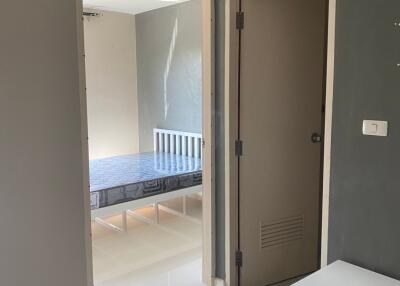 View into a bedroom from an adjacent room, showing a bed and part of a nightstand.