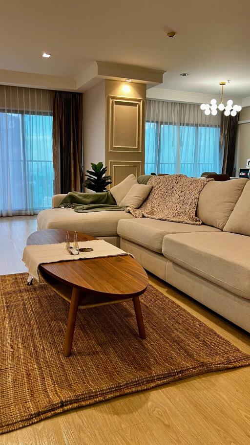 Modern living room with beige sectional sofa, wooden coffee table, and large windows