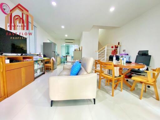 Modern living area with beige sofa, wooden dining table, and open staircase