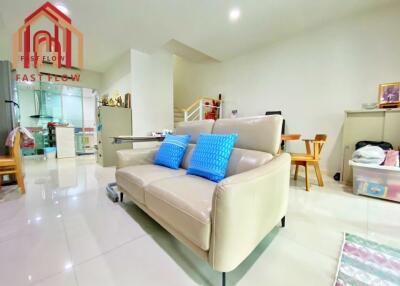 White themed living room with a beige sofa, blue pillows, and adjacent kitchen.