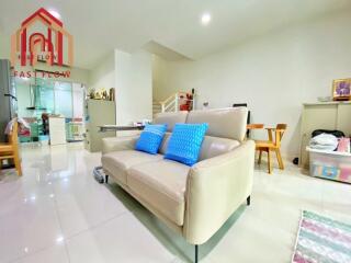 White themed living room with a beige sofa, blue pillows, and adjacent kitchen.