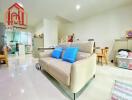 White themed living room with a beige sofa, blue pillows, and adjacent kitchen.