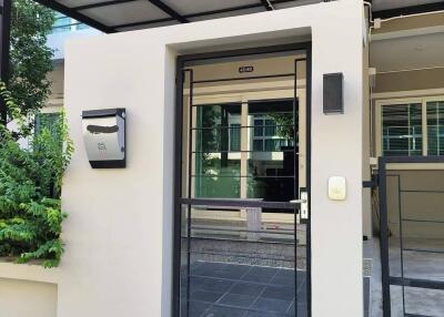 Front entrance of a modern house with a small garden, mailbox, and black metal gate