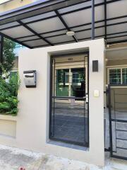 Front entrance of a modern house with a small garden, mailbox, and black metal gate