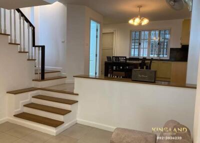 View of living room with staircase leading to upper floor, adjacent dining area, and kitchen in background.