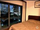 Night-time view of bedroom with large window overlooking cityscape