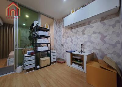 A small cluttered bedroom with wallpaper, wooden floors, and built-in cabinets