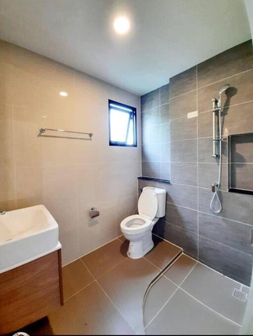 Modern bathroom with tiled walls, a toilet, a sink, and a window